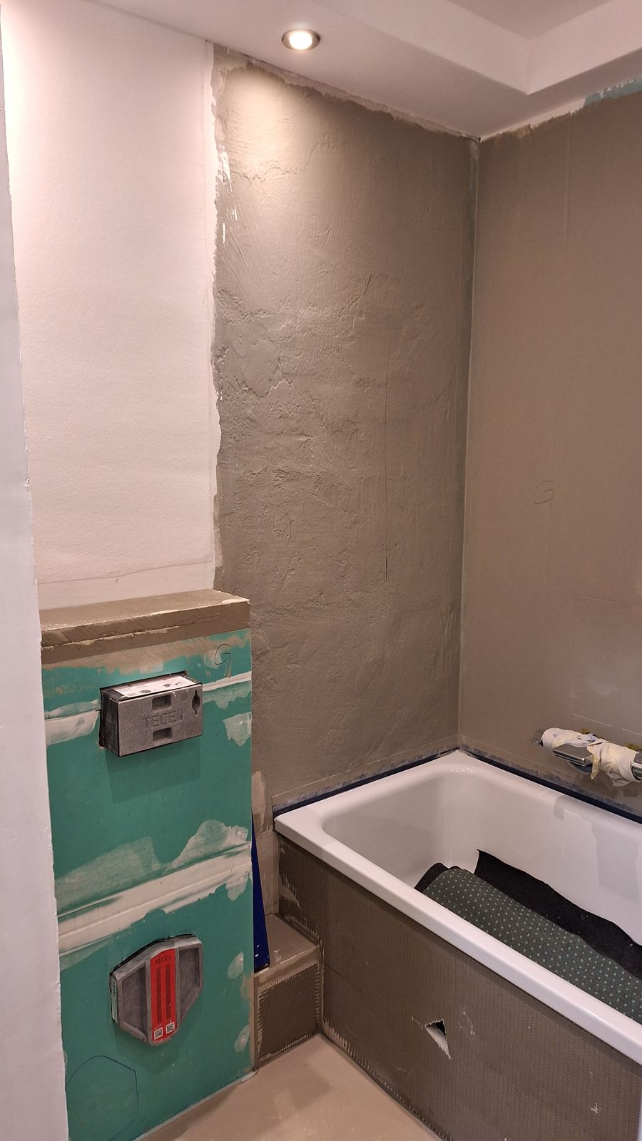Vorwand für ein Hänge-WC mit grünen imprägnierten Gipsplatten, Spülkasten-Revisionsöffnung und Betätigungsplatte, daneben frisch verputzte Wand